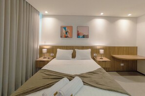 A hotel room with a large bed, two bedside tables, a wooden headboard, and two wall-mounted artworks.