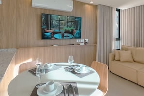 A modern living room with a dining area, a flat-screen TV mounted on the wall, and a sofa. - Modern Downtown Apartment with Style - NEO1004 (Maringá)