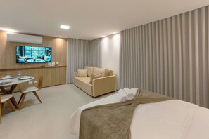 Een hotelkamer met een bed, een bank, een televisie en een eethoek.