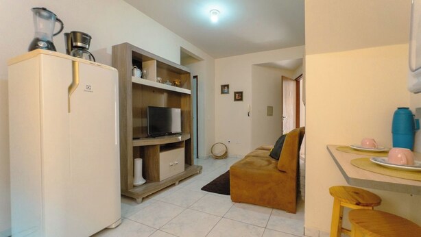 Espaço compacto com cozinha compacta, sofá, área de refeições e painel de entretenimento embutido.