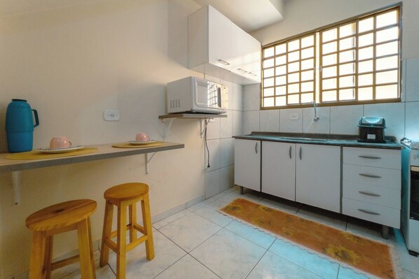 A small kitchen with white cabinets, a microwave, a sink, and a window with a grid pattern.