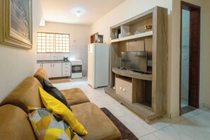 A living room with a sofa, a television, and a kitchen area in the background.