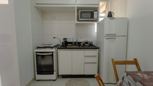 Cocina compacta con gabinetes blancos, microondas, estufa y refrigerador.