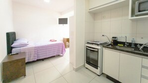 Habitación de hotel compacta con cama, kitchenette y televisor de pantalla plana montado en la pared.