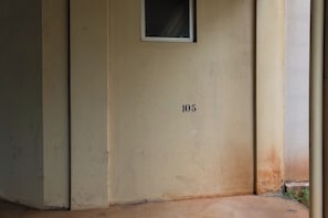 Pared beige con el número 105, una ventana pequeña y un piso de concreto.