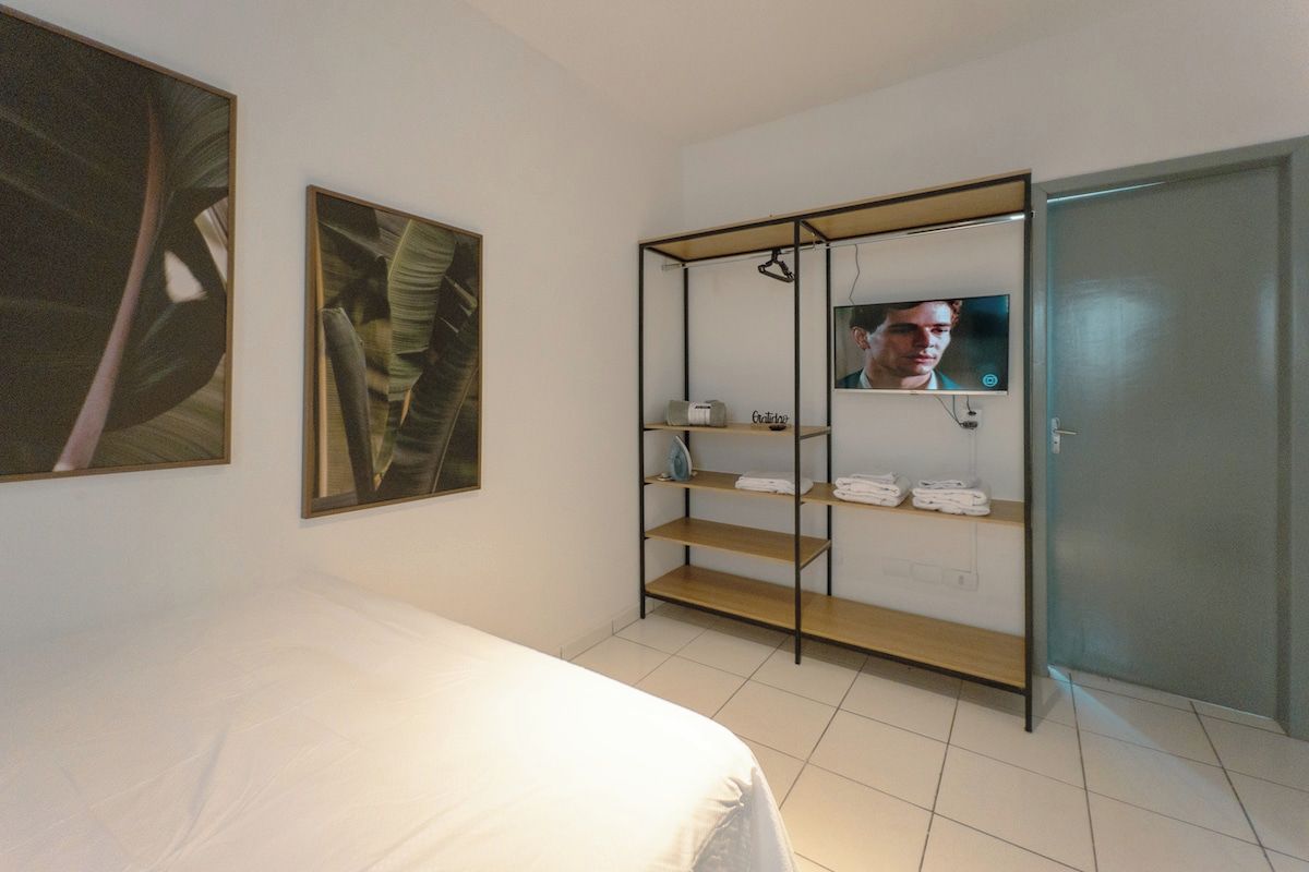 Quarto de hotel com cama, armário com prateleiras e televisão.