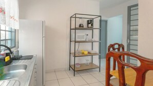 Cuina amb un rentaplatets d'acer inoxidable, un frigorífic blanc, una cadira de fusta i un moble prestatgeria metàl·lica amb diversos objectes.