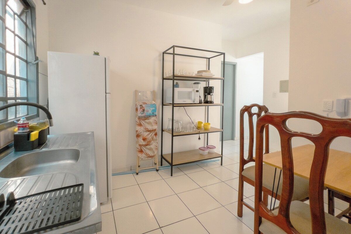 Cozinha equipada com geladeira, micro-ondas, cafeteira e prateleira com louças.