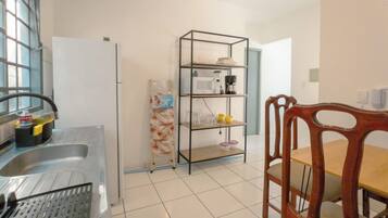 Cozinha equipada com geladeira, micro-ondas, cafeteira e prateleira com louças.
