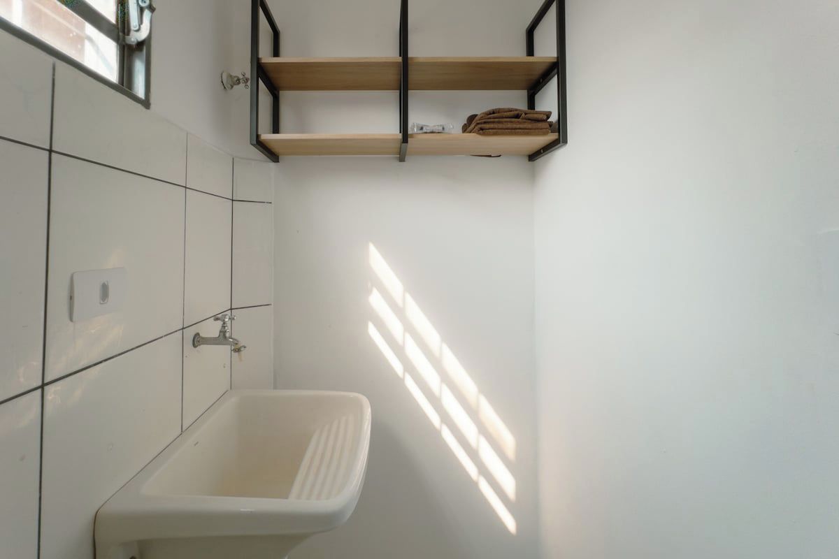 Un baño con un lavamanos blanco, un perchero y un ventanal que permite la entrada de luz natural.