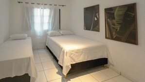 Un dormitori amb dos llits, una finestra amb cortines lleugeres i dos quadres al mur.