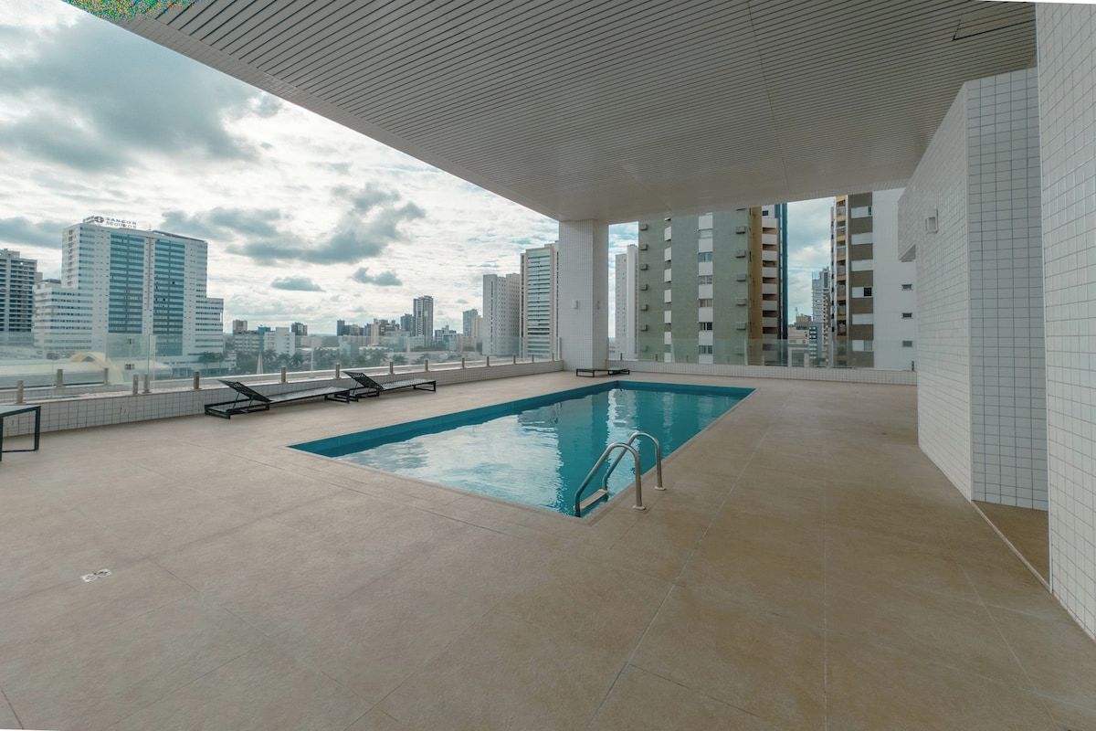 Ein Dachpool mit Blick auf die Stadt, umgeben von einer gefliesten Terrasse und Liegestühlen.