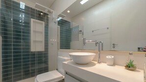 Un bany modern amb dutxa d'ús de vidre, un vàter blanc, un rentapeus amb un gran mirall a sobre i una petita planta al taulell.