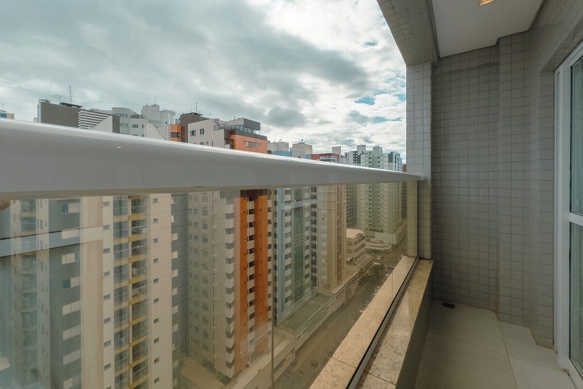 A balcony with a view of high-rise buildings, a tiled wall, and a glass door.