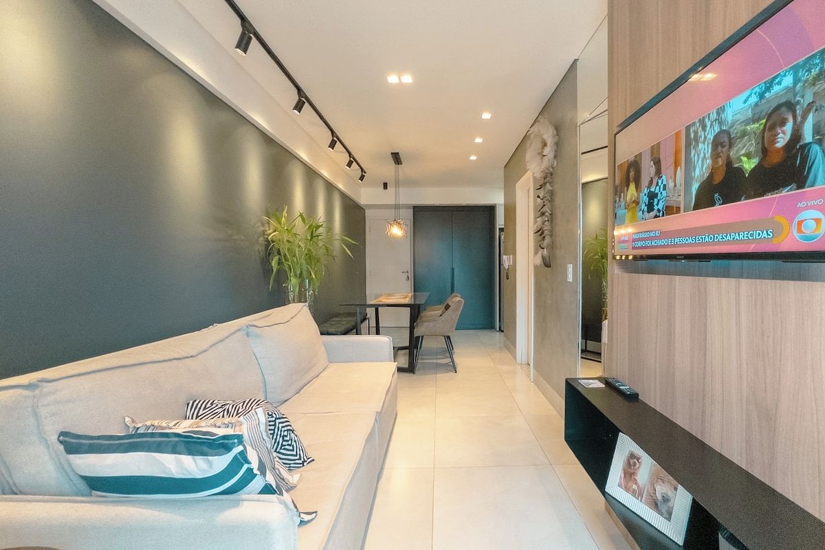 A modern living room with a sofa, a dining area, and a flat-screen TV mounted on the wall.