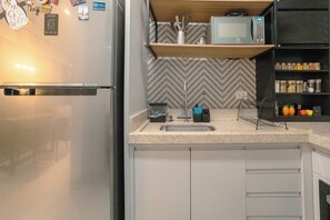 A kitchen with a built-in microwave, a sink, and a wooden shelf above it. - Comfortable Apartment in Maringa - JR1207 (Maringá)