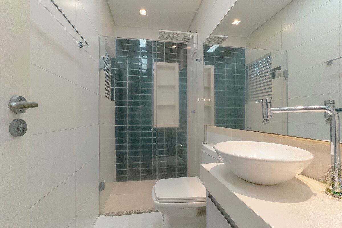 Un baño moderno con ducha envuelta en vidrio, un lavamanos blanco y un inodoro.