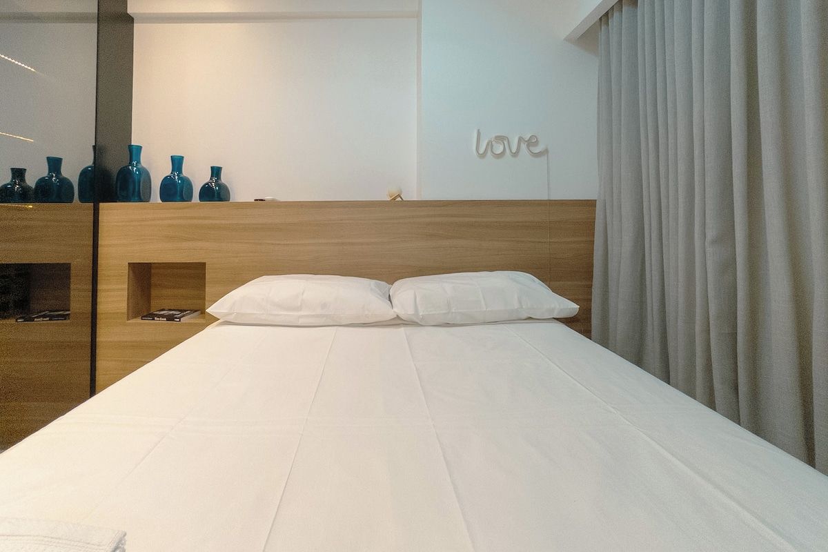 Ein modernes Hotelzimmer mit einem Holzkopfstück, weißer Bettwäsche und einem an der Wand befestigten Spiegel.
