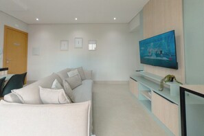 Un salón moderno con un sofá, un televisor de pantalla plana montado en la pared y una planta pequeña en una estantería.