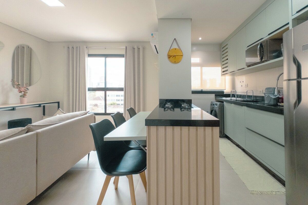 Een moderne keuken met een centraal eiland, een zithoek met een bank en stoelen, en een groot raam met gordijnen.