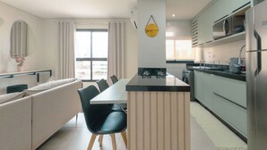 Cozinha moderna com ilha central, área de refeições com sofá e cadeiras, e uma grande janela que ilumina naturalmente o espaço.