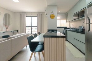 Een moderne keuken met een centraal eiland, een zithoek met een bank en stoelen, en een groot raam dat voor natuurlijk licht zorgt.