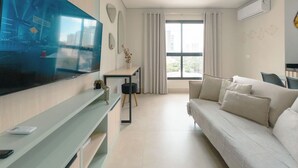 Uma sala de estar moderna com uma televisão de tela grande, um sofá, uma mesa pequena e uma janela com cortinas.