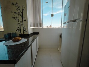 Cozinha compacta com bancada preta, adesivo de parede de bambu e vista da cidade pela janela.