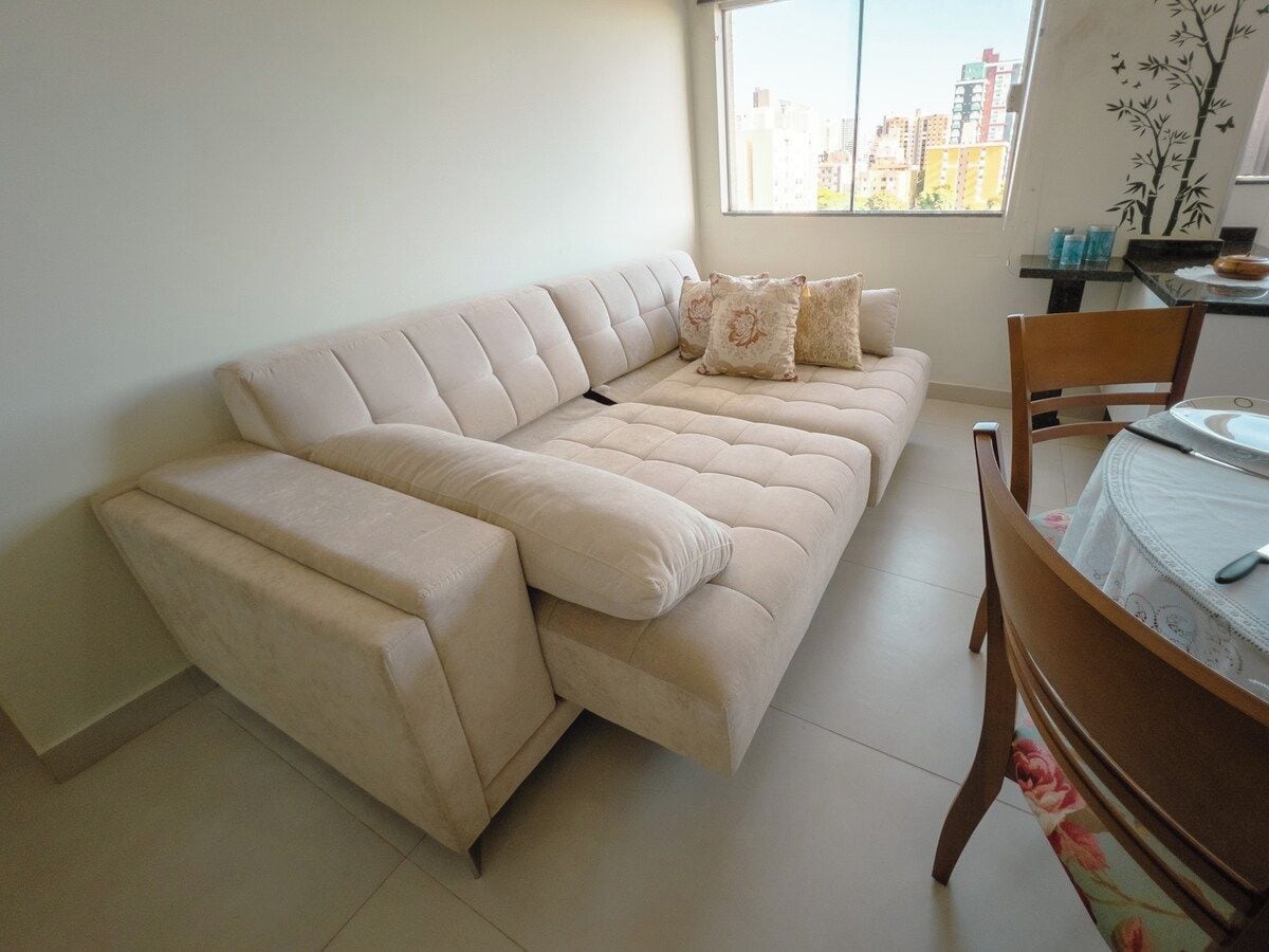 Ein beiges Sofa mit Chaiselongue, ein Esstisch mit Stühlen und ein Fenster mit Blick auf die Stadt.