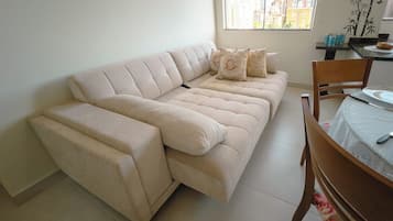 Ein beiges Sofa mit Chaiselongue, ein Esstisch mit Stühlen und ein Fenster mit Blick auf die Stadt.