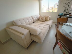 Um sofá bege com chaise, uma mesa de jantar com cadeiras e uma janela com vista para a cidade.