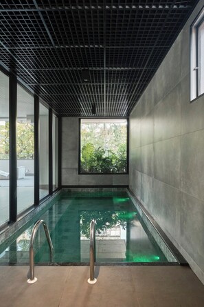 Piscina interior moderna com teto em padrão quadriculado, grandes janelas e vista para o verde lá fora.