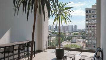 A balcony with a potted palm tree, a dining table with chairs, and a view of a cityscape.