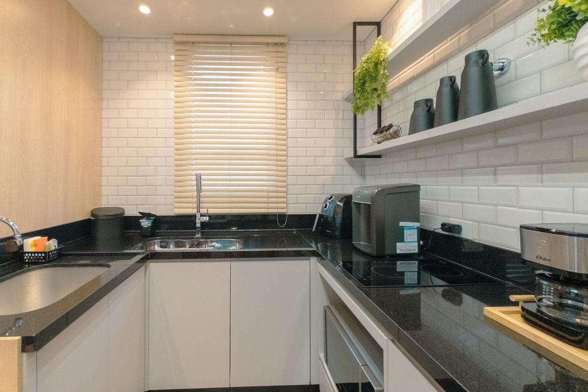 Uma cozinha moderna com azulejos brancos, bancada preta, forno embutido e máquina de café.