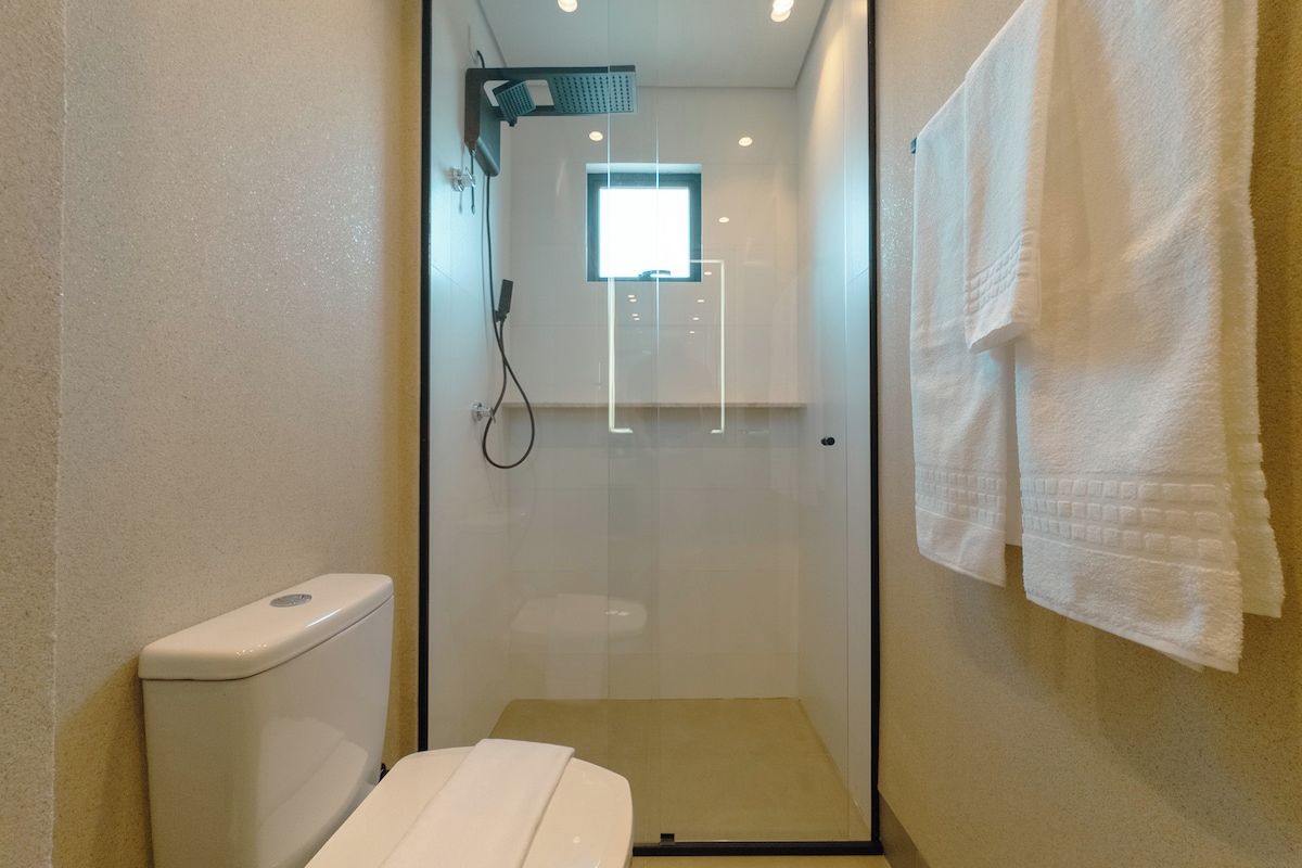 Box de vidro com chuveiro, vaso sanitário e porta-toalhas.