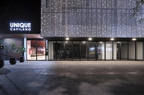 En modern byggnad med en stor, upplyst skylt som visar texten ”UNIQUE CAPILANO” och en rymlig entré.