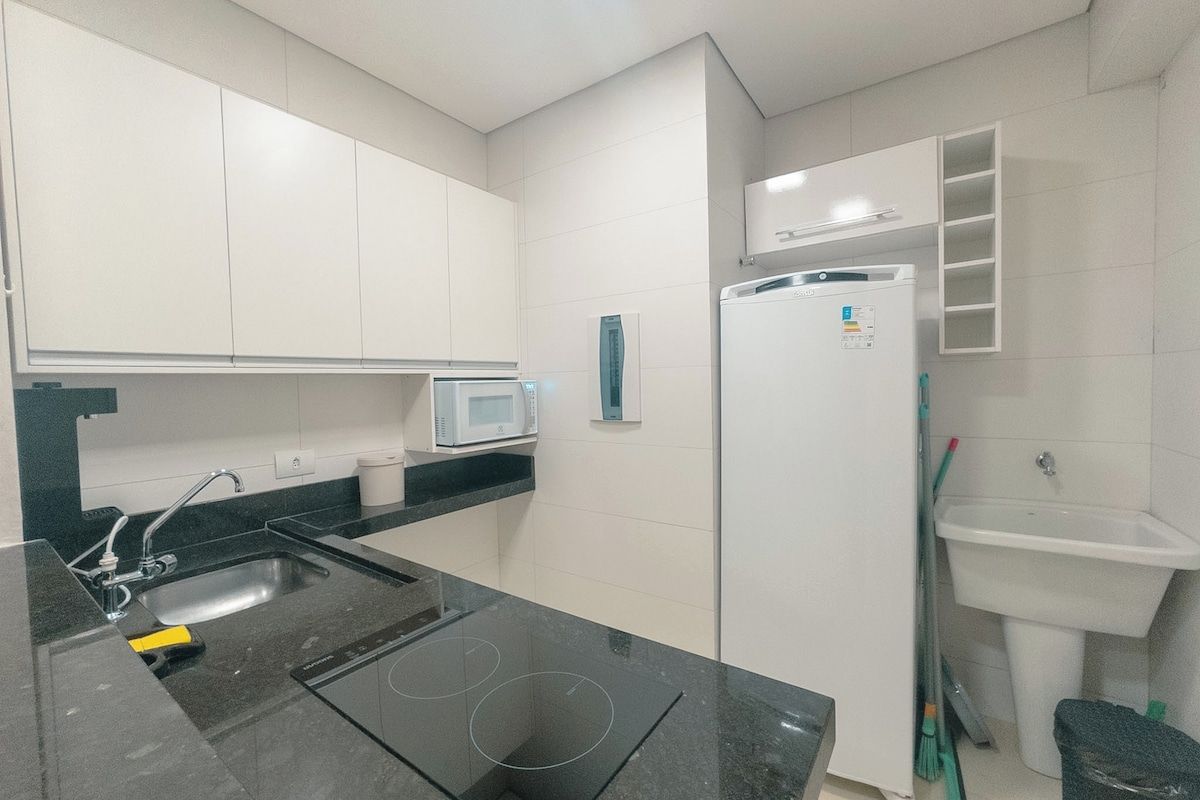 Una cocina moderna con encimera negra, armarios blancos, un microondas, un refrigerador y un lavaplatos.