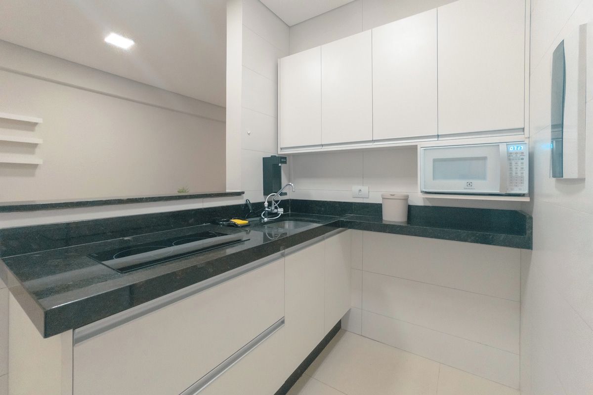 A modern kitchen with white cabinets, a black countertop, a built-in microwave, and a stainless steel sink.