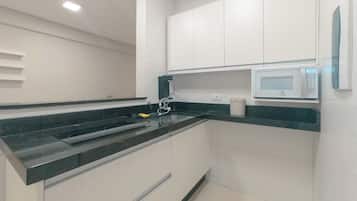 A modern kitchen with white cabinets, a black countertop, a built-in microwave, and a stainless steel sink.