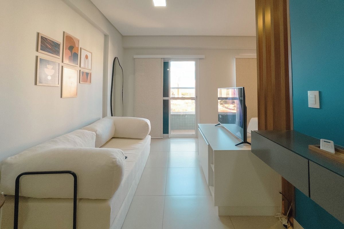 A modern hotel room with a sofa, a desk, and a refrigerator.