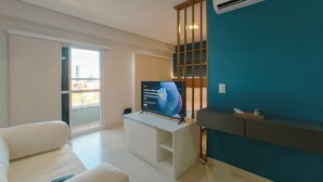 A modern living room with a flat-screen TV on a white stand, a sofa, a sliding glass door leading to a balcony, and a teal accent wall. - Top Location in the Heart of Maringa - JR509 (Maringá)