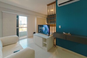 Ein modernes Wohnzimmer mit einem Flachbildfernseher auf einem weißen Schrank, einer Couch, einer Schiebetür zum Balkon und einer Wand in Türkis.