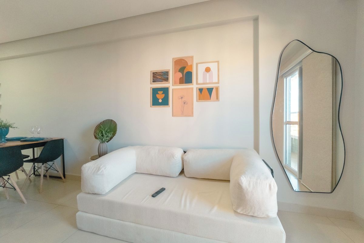 Una habitación moderna con un sofá blanco, una mesa de comedor con sillas, una pequeña planta en maceta y arte abstracto en la pared.
