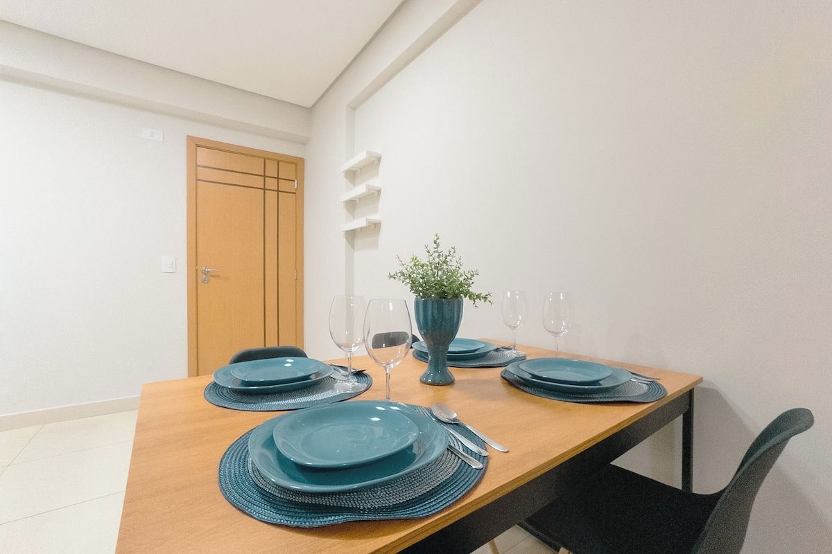 A dining table set with blue plates, glasses, and a vase with a plant.