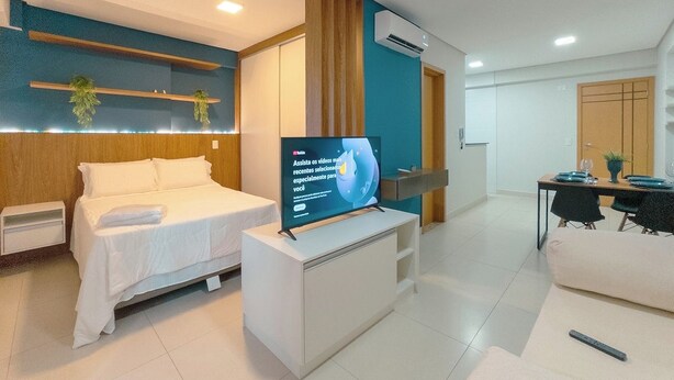 A modern hotel room with a bed, a TV on a stand, a dining table with chairs, and a sofa. - Top Location in the Heart of Maringa - JR509 (Maringá)