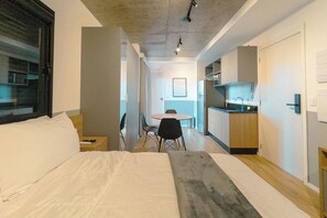 Ein modernes Hotelzimmer mit einem großen Bett, einem kleinen Schreibtisch, einer Essecke mit Stühlen und einer Küchenzeile.