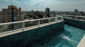 Piscina no terraço com vista para a paisagem urbana, cercada por edifícios.