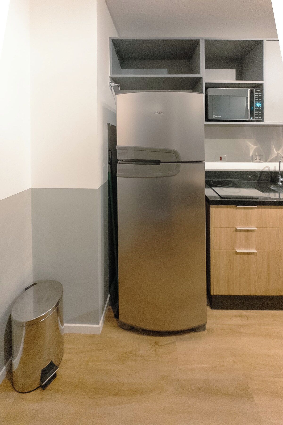 A compact kitchen with a stainless steel refrigerator, a microwave, and wooden cabinets.