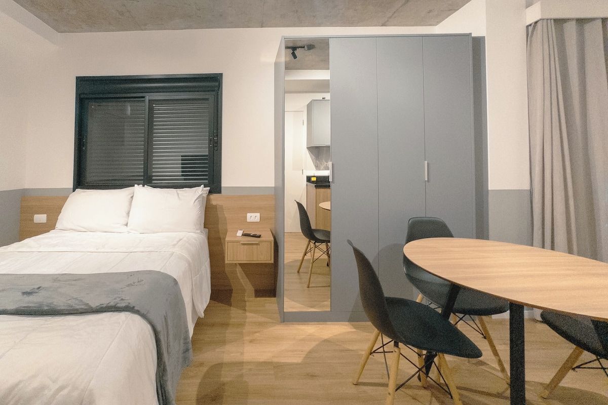 Habitació d'hotel amb llit, taula de nit, escriptori i zona de menjador amb cadires.