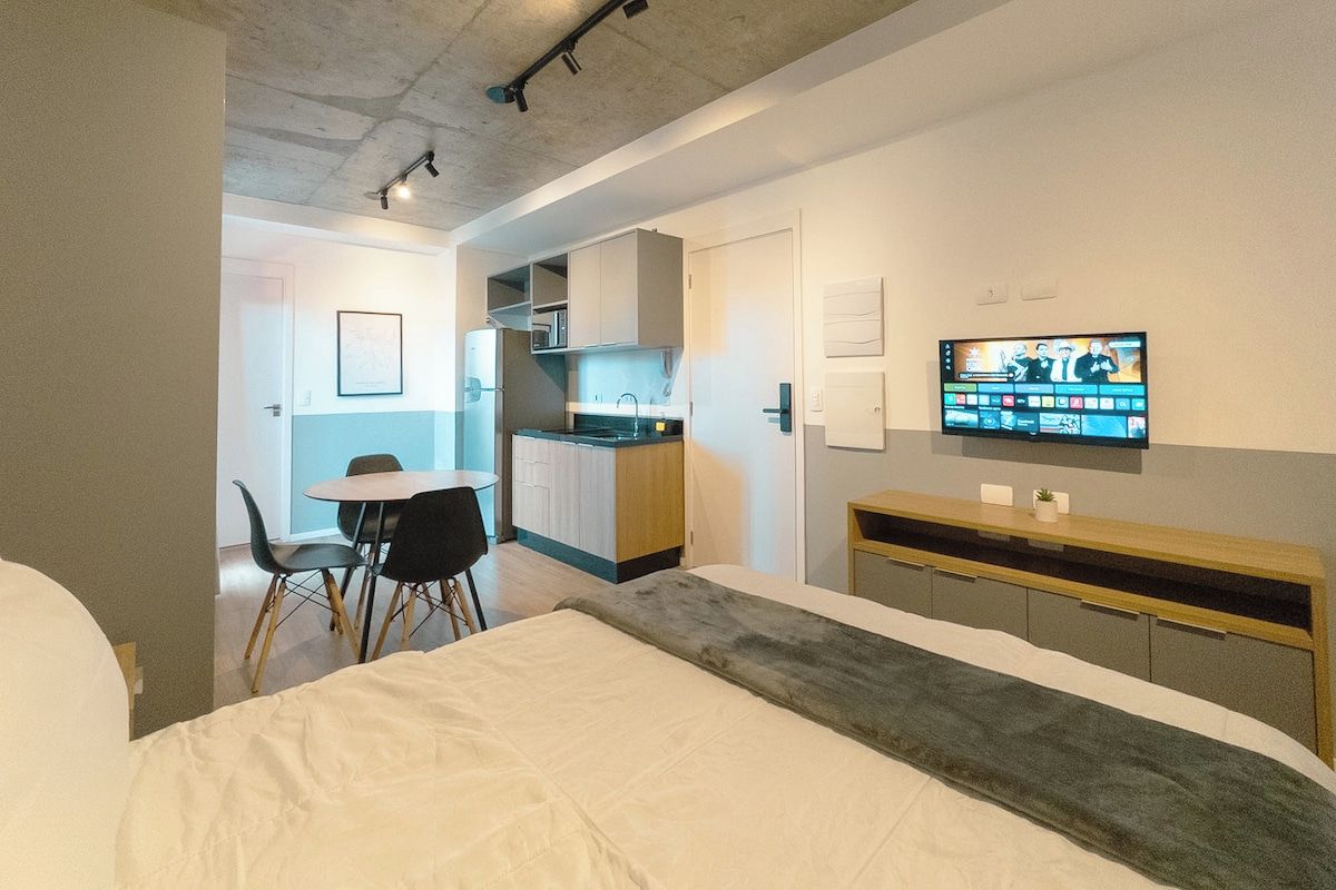 Una habitación de hotel moderna con cama, televisión, escritorio y kitchenette.